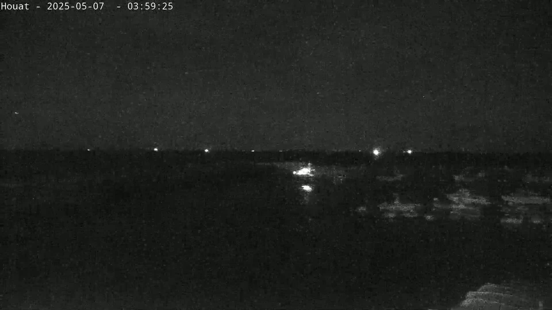 A nighttime, low-light view of a dark landscape with a few distant lights visible on the horizon.
