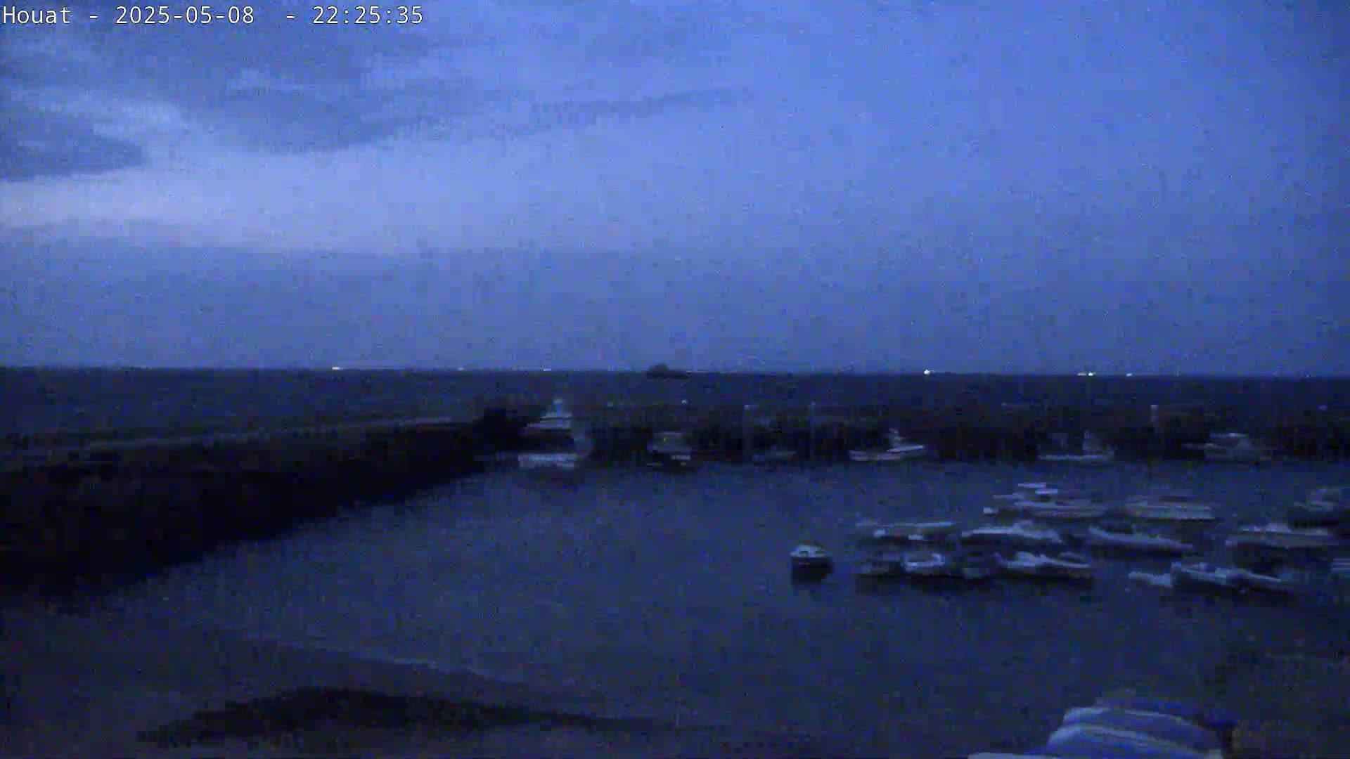 A harbor filled with numerous boats is visible under a dark, twilight sky.
