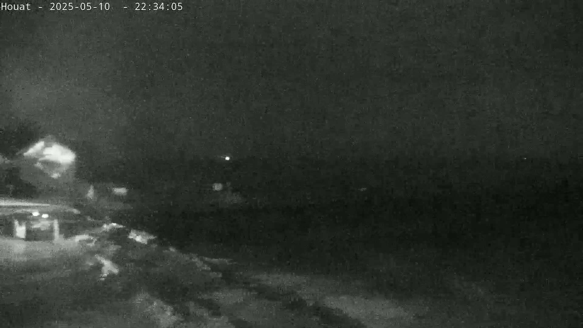 A nighttime, low-light image shows a dark, indistinct landscape with a few faint lights visible in the distance.