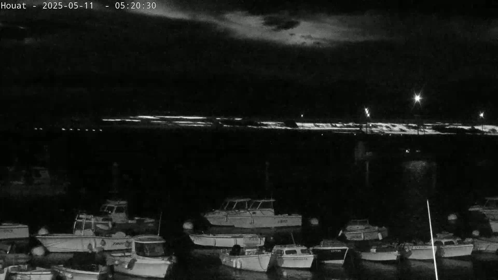 A nighttime, low-light view of a harbor filled with numerous small boats under a partly cloudy sky.