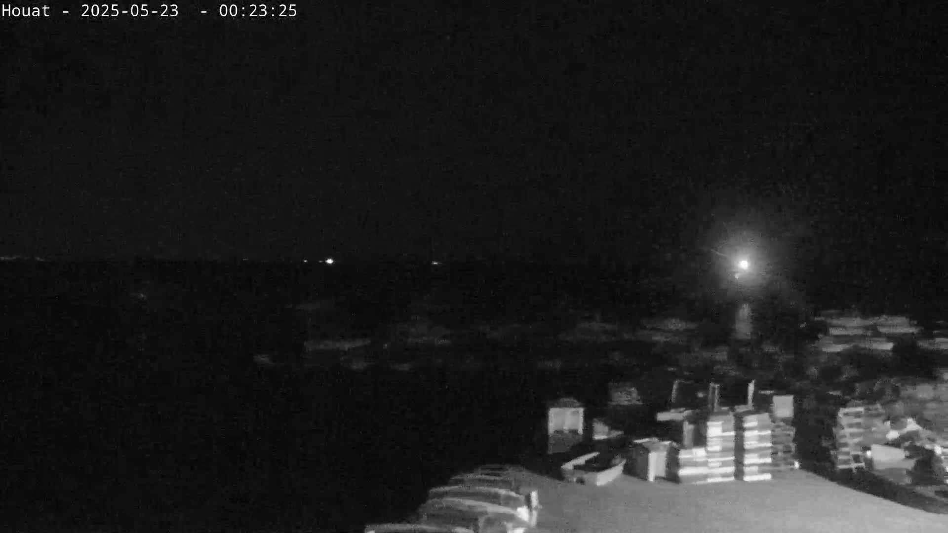 A nighttime, low-light image shows a dark landscape with indistinct objects in the foreground and a few distant lights visible on the horizon.