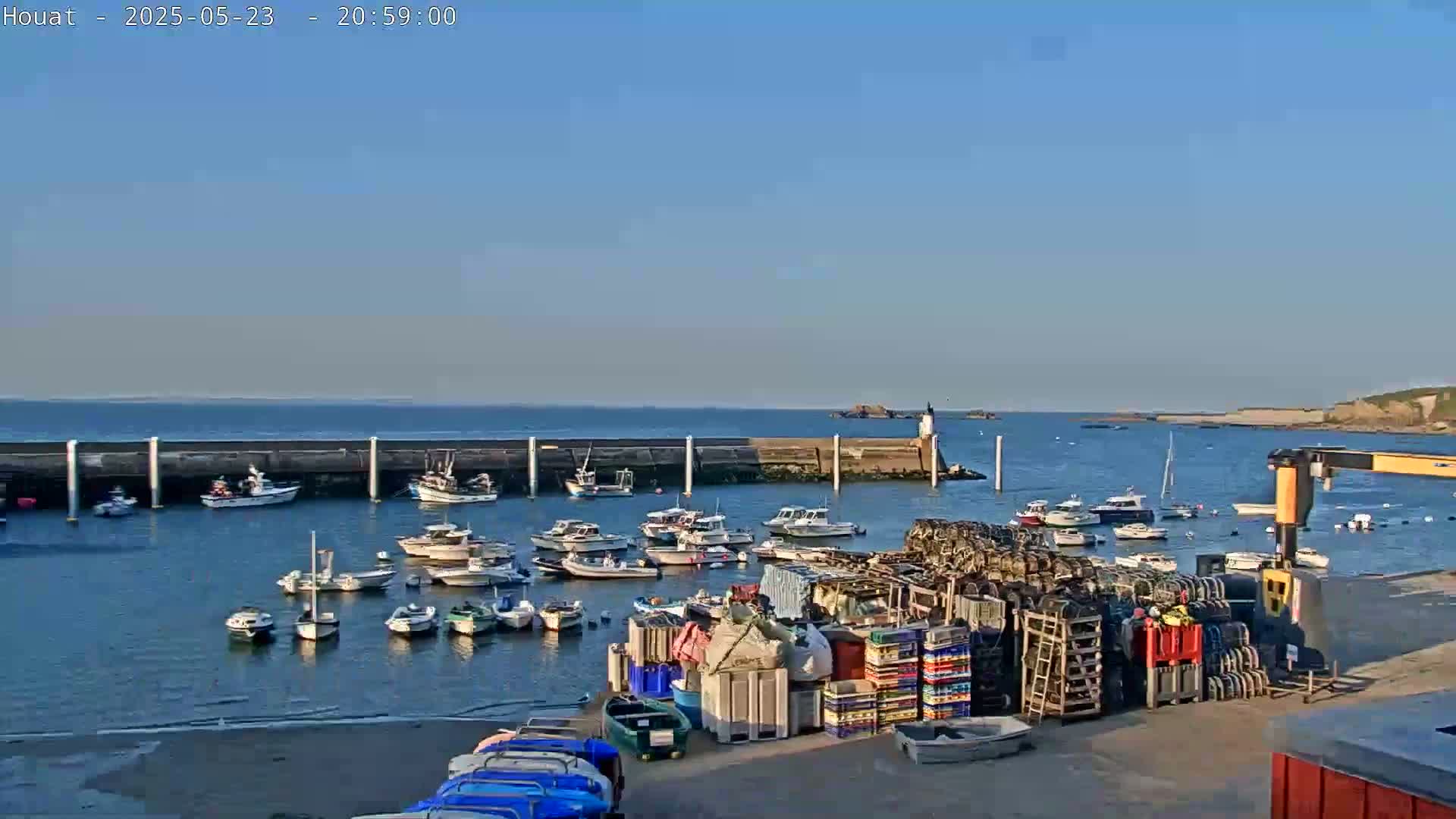 A harbor filled with numerous boats is situated beside a stone wall, under a clear blue sky.