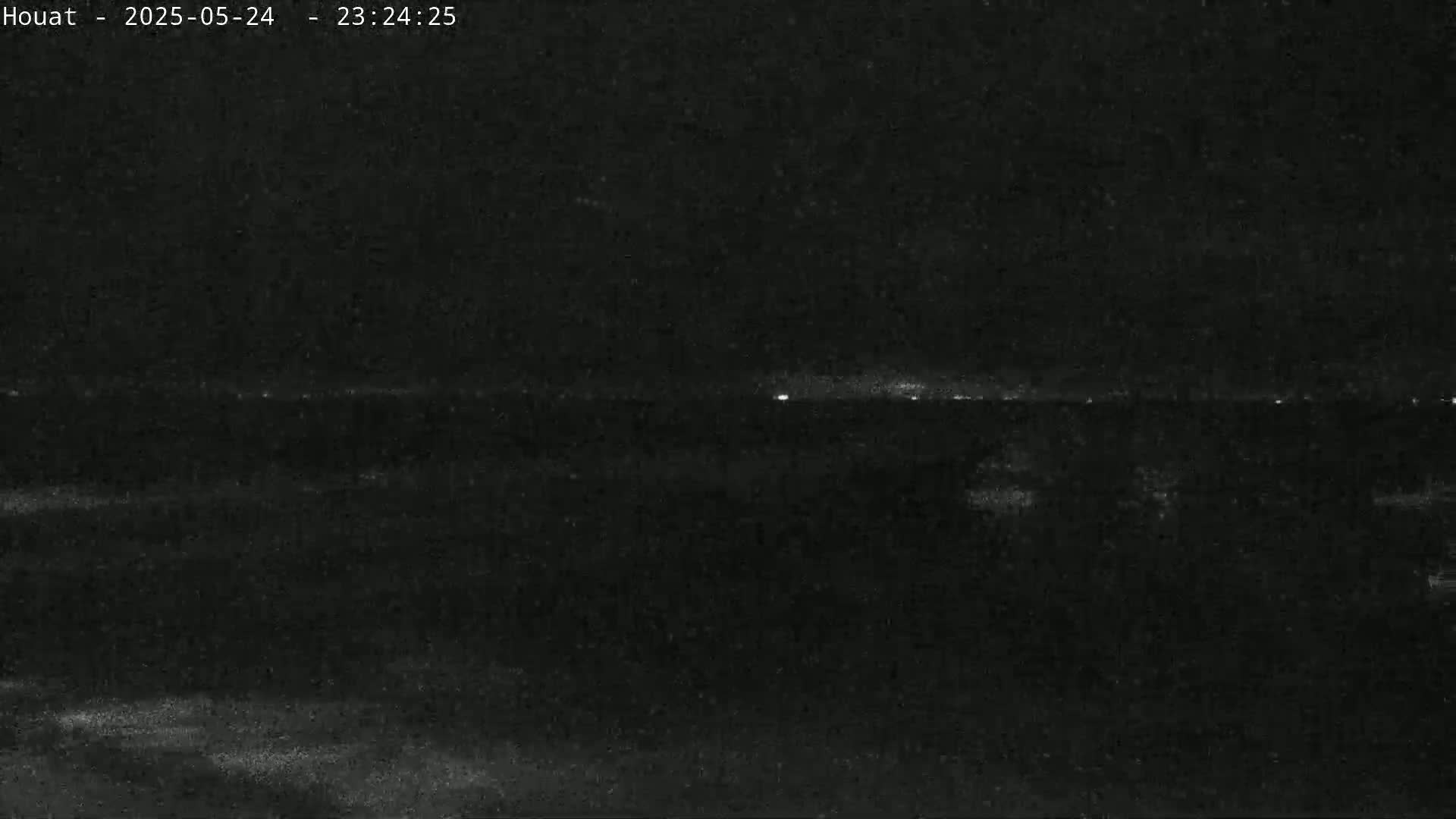A nighttime long shot shows a dark, possibly coastal, landscape with a faint horizon line illuminated by distant lights.