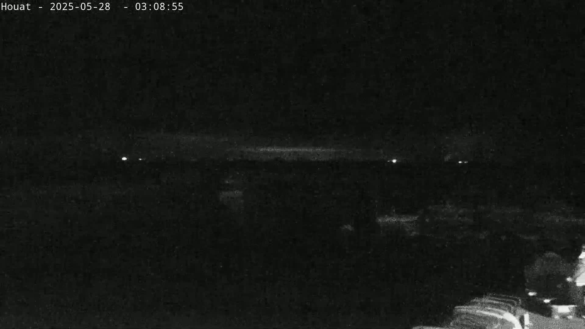 A nighttime, low-light image shows a dark, flat landscape with a few faint lights in the distance.