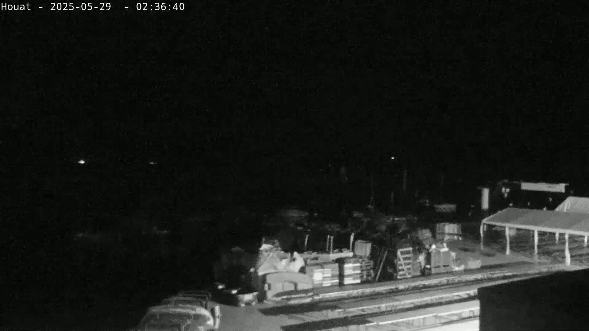 A nighttime, low-light view of a dark area with some structures, vehicles, and what appears to be a large tent.
