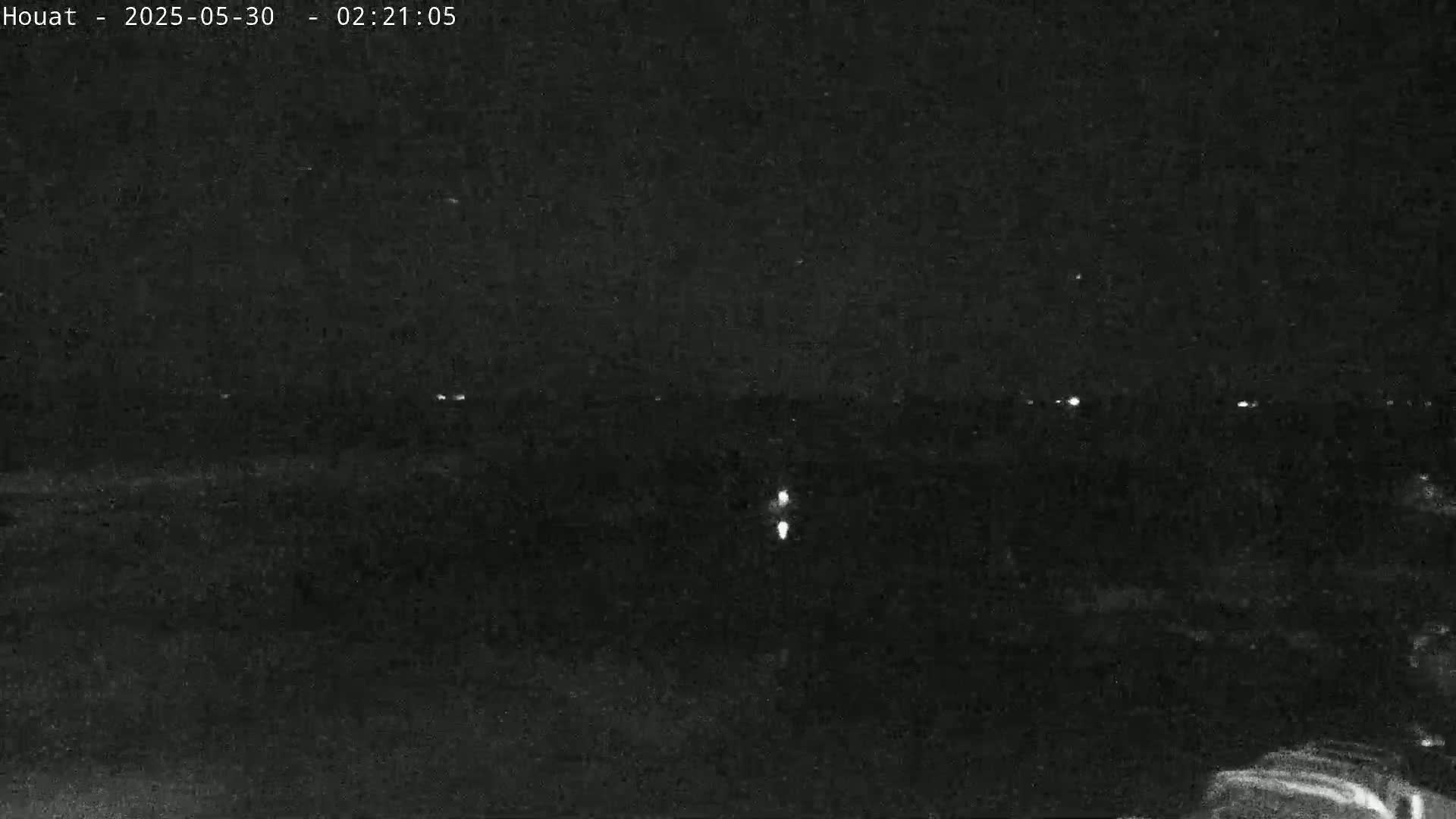 A nighttime, low-light view shows a dark landscape with a few distant lights and two brighter lights closer to the camera.