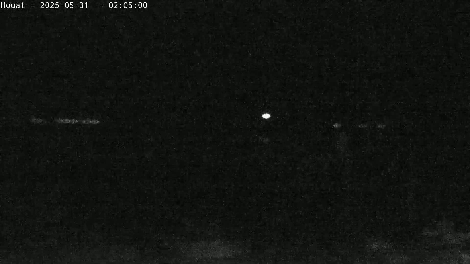 A nighttime, low-light image shows a few faint lights in the distance against a dark background.