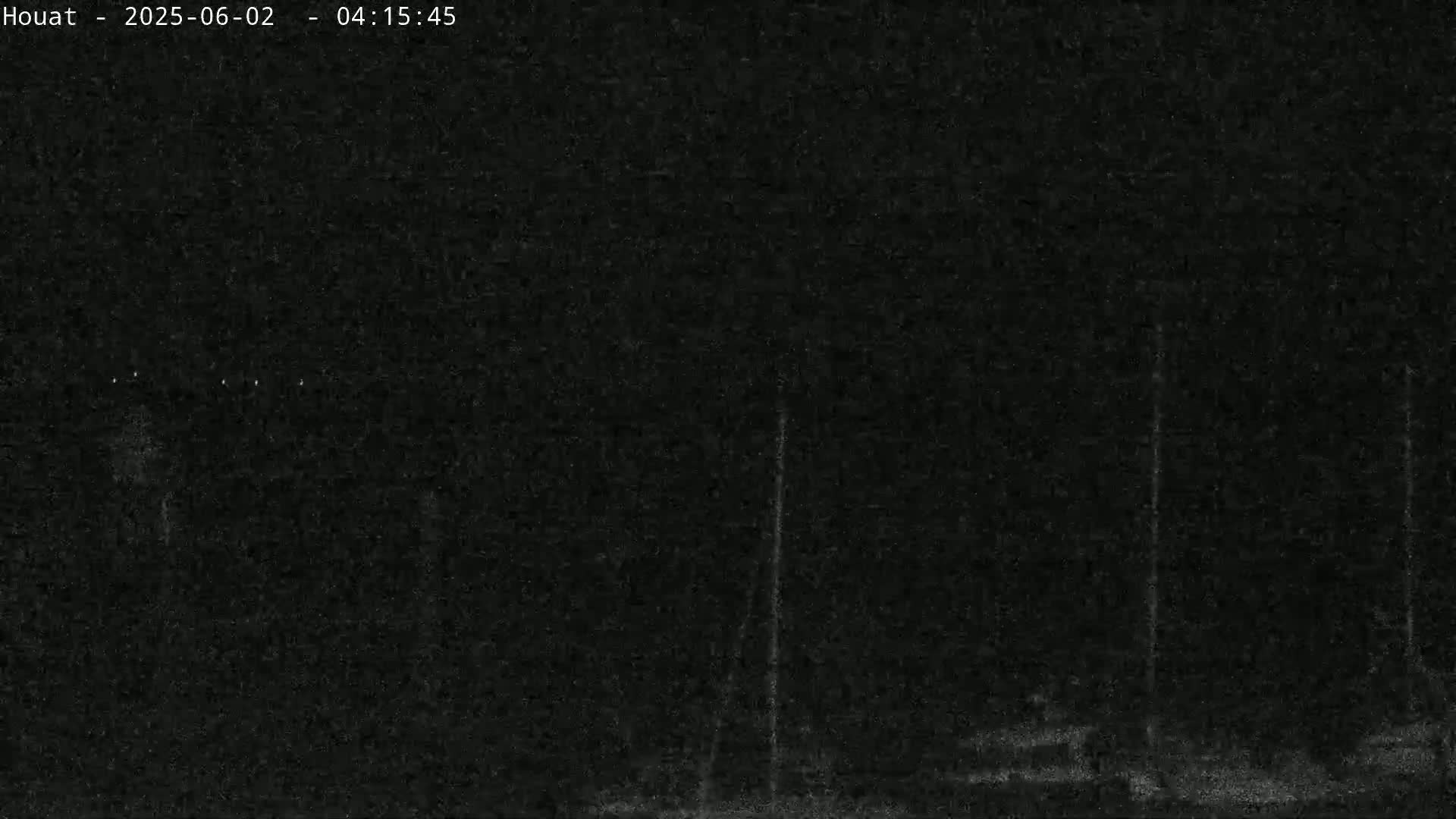 A dark, nighttime image shows indistinct objects that appear to be tall, thin poles or masts silhouetted against a very dark sky.