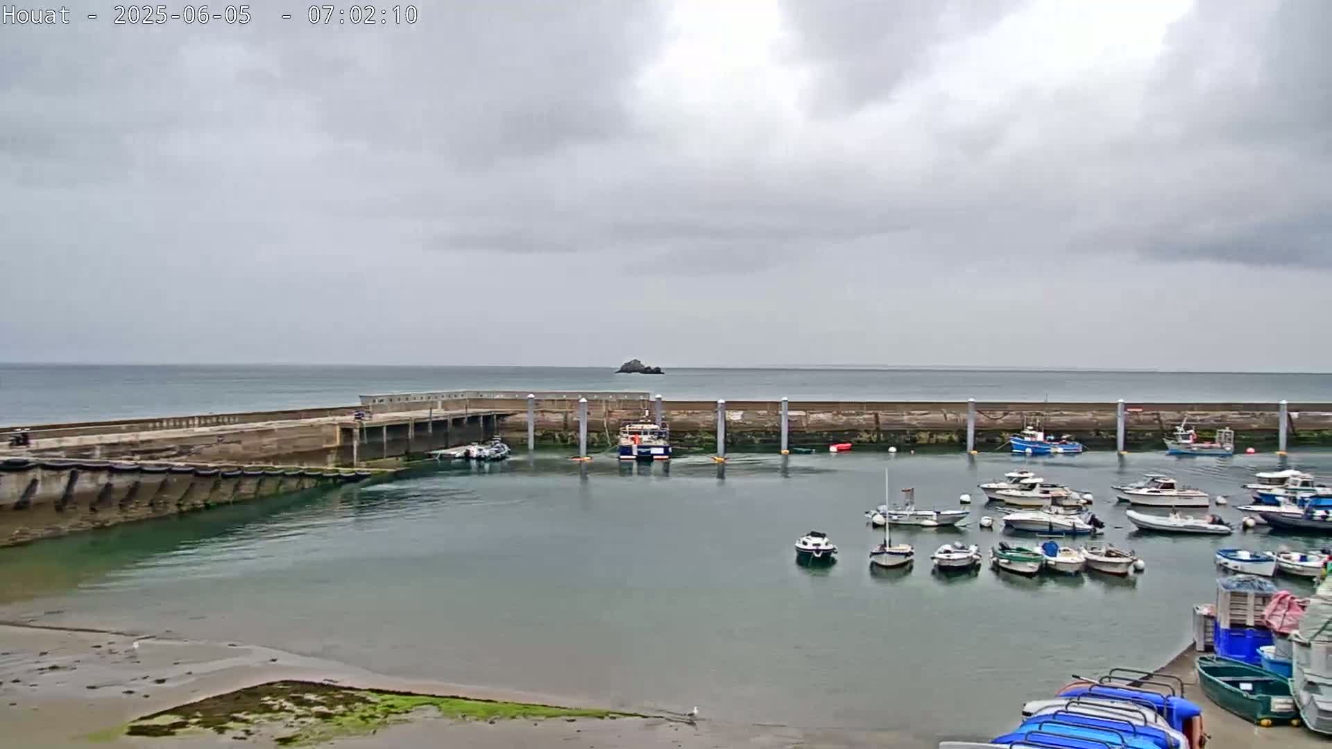 A harbor filled with numerous boats is situated next to a sea wall under an overcast sky.
