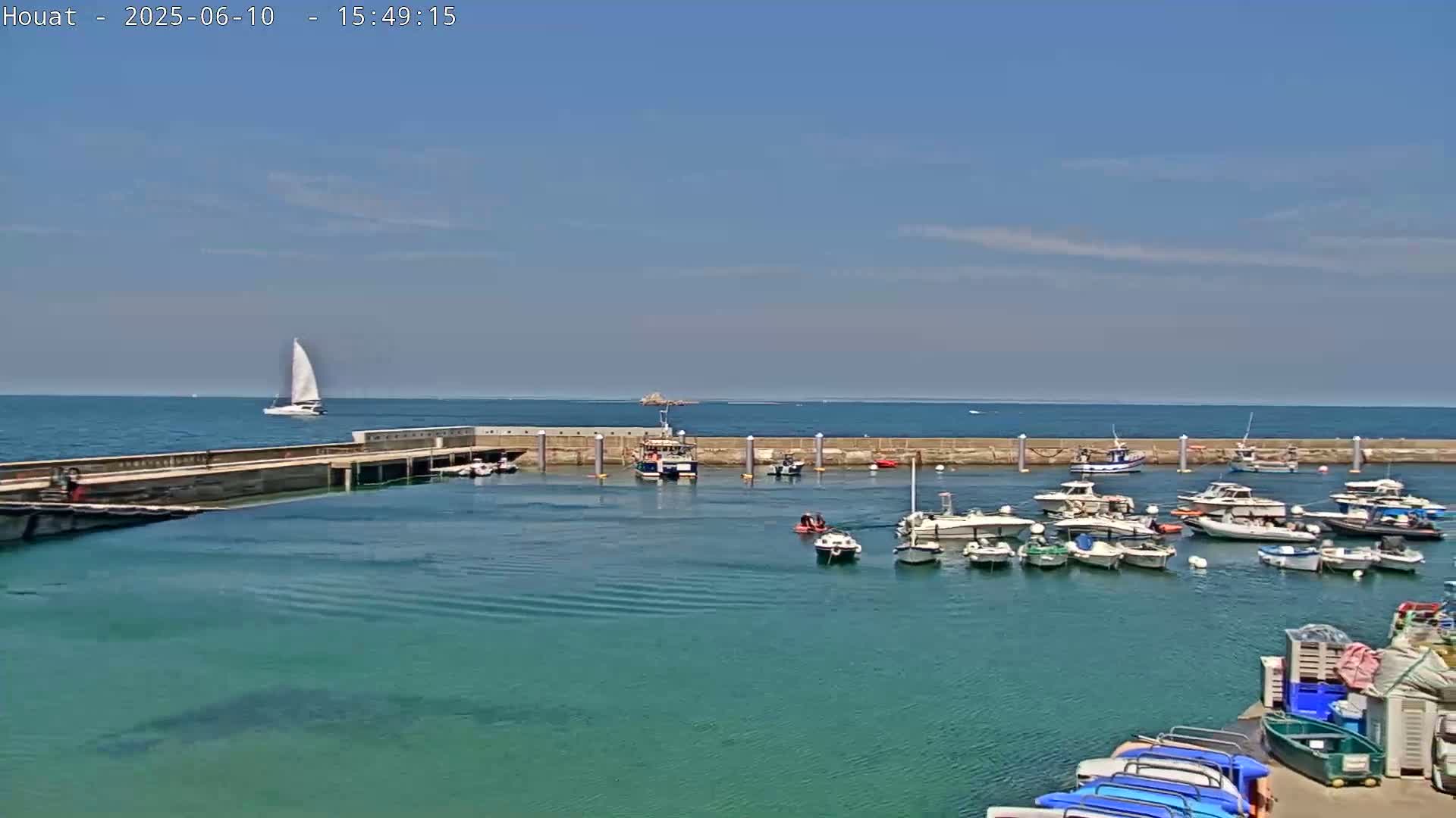 A harbor filled with numerous boats under a clear blue sky, with a sailboat visible in the distance.