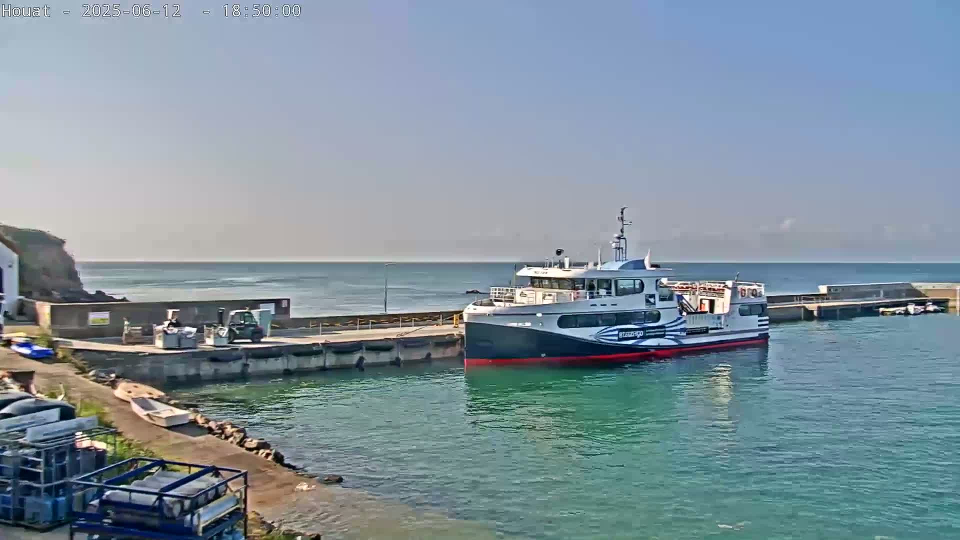 A ferry is docked at a pier on a calm, sunny day next to a rocky shoreline.