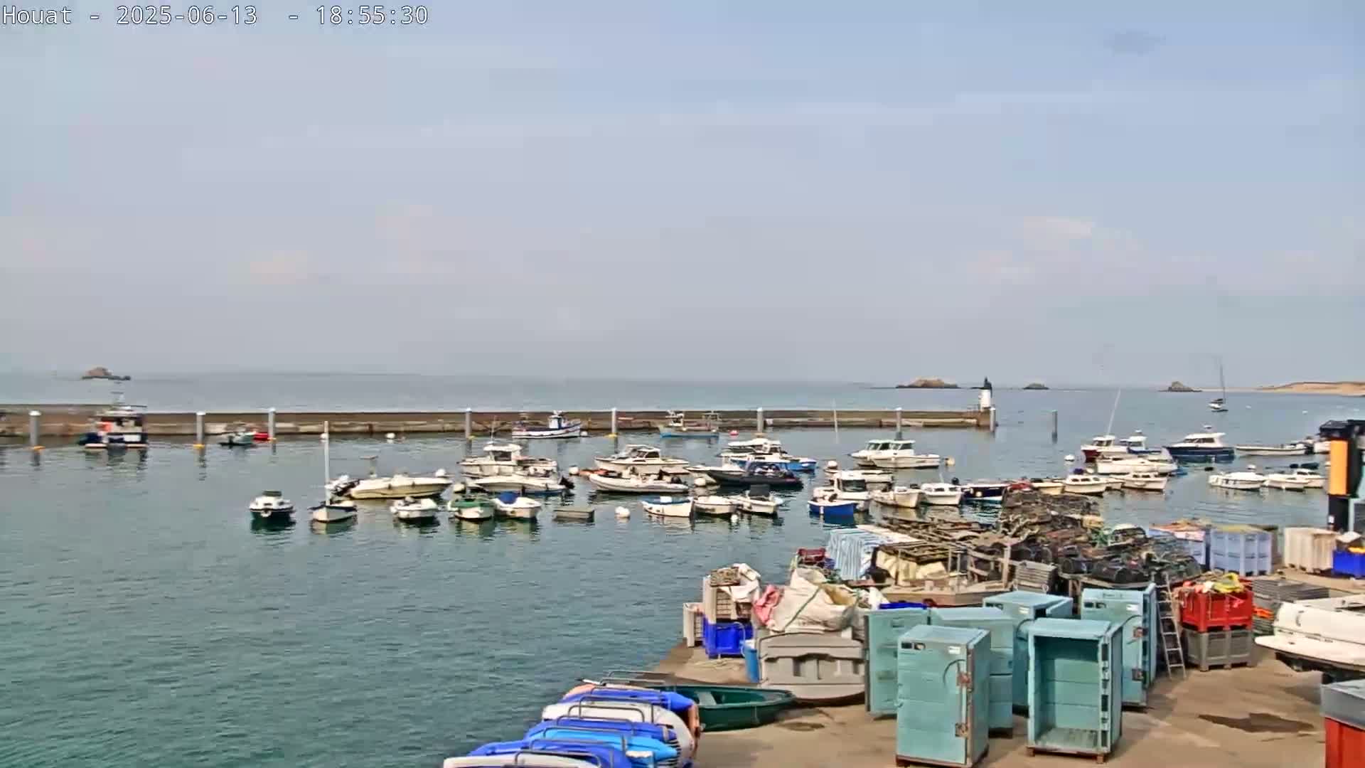 A harbor filled with numerous boats is shown on a mostly clear day, with a calm sea extending to distant islands.