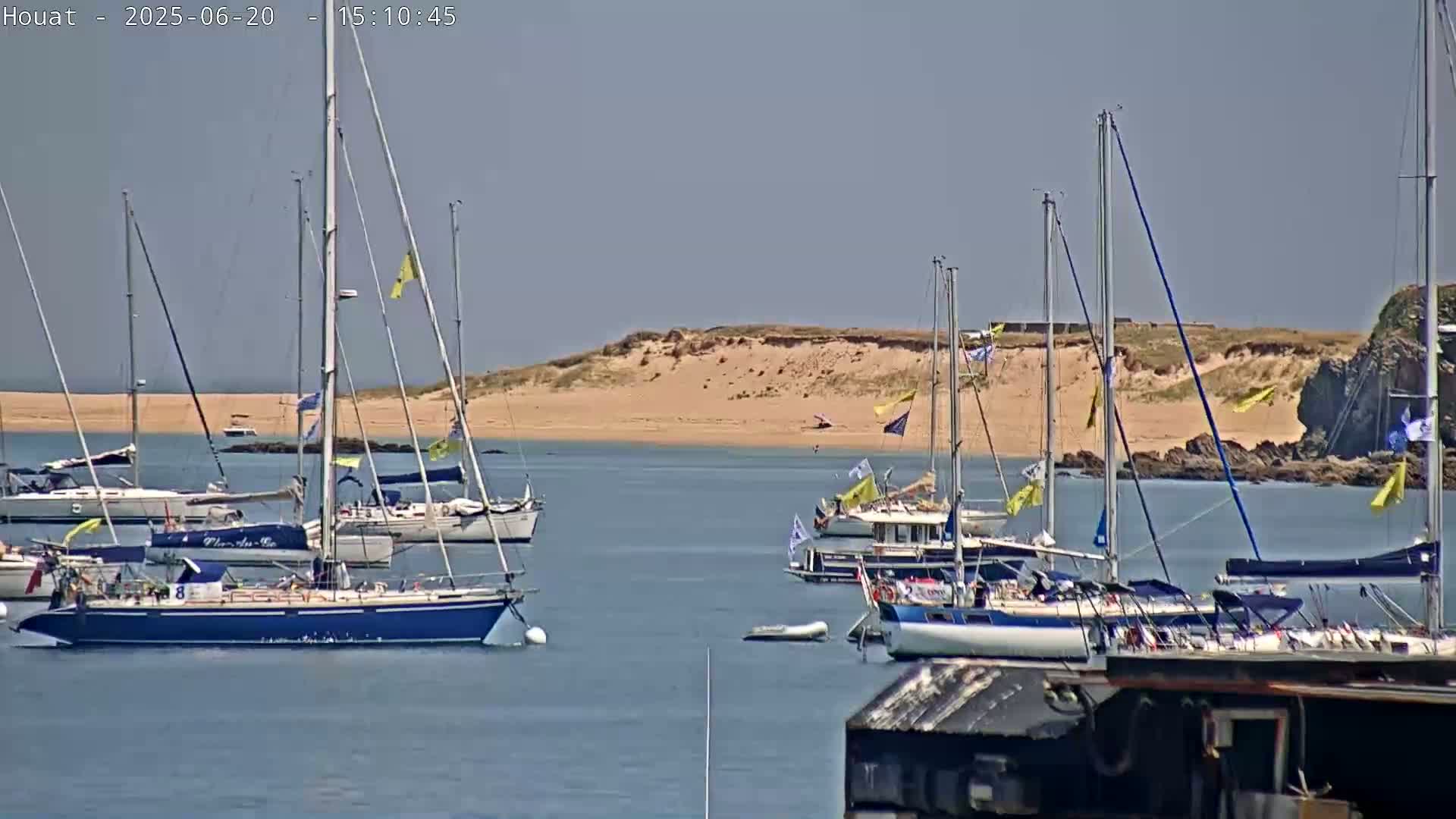 Several sailboats are moored in calm water near a sandy shore on a sunny day.