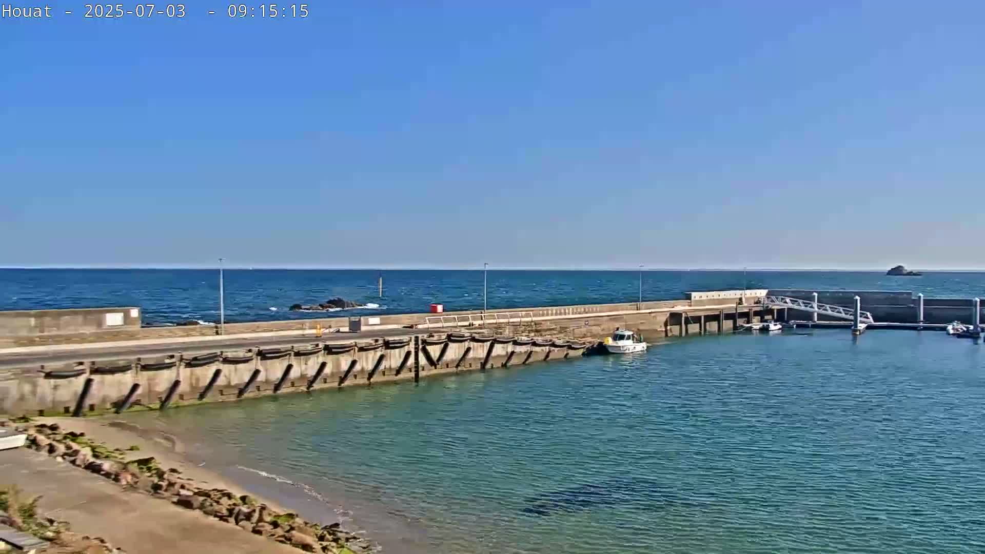 A small harbor with a few boats is seen on a sunny day with calm, blue water.