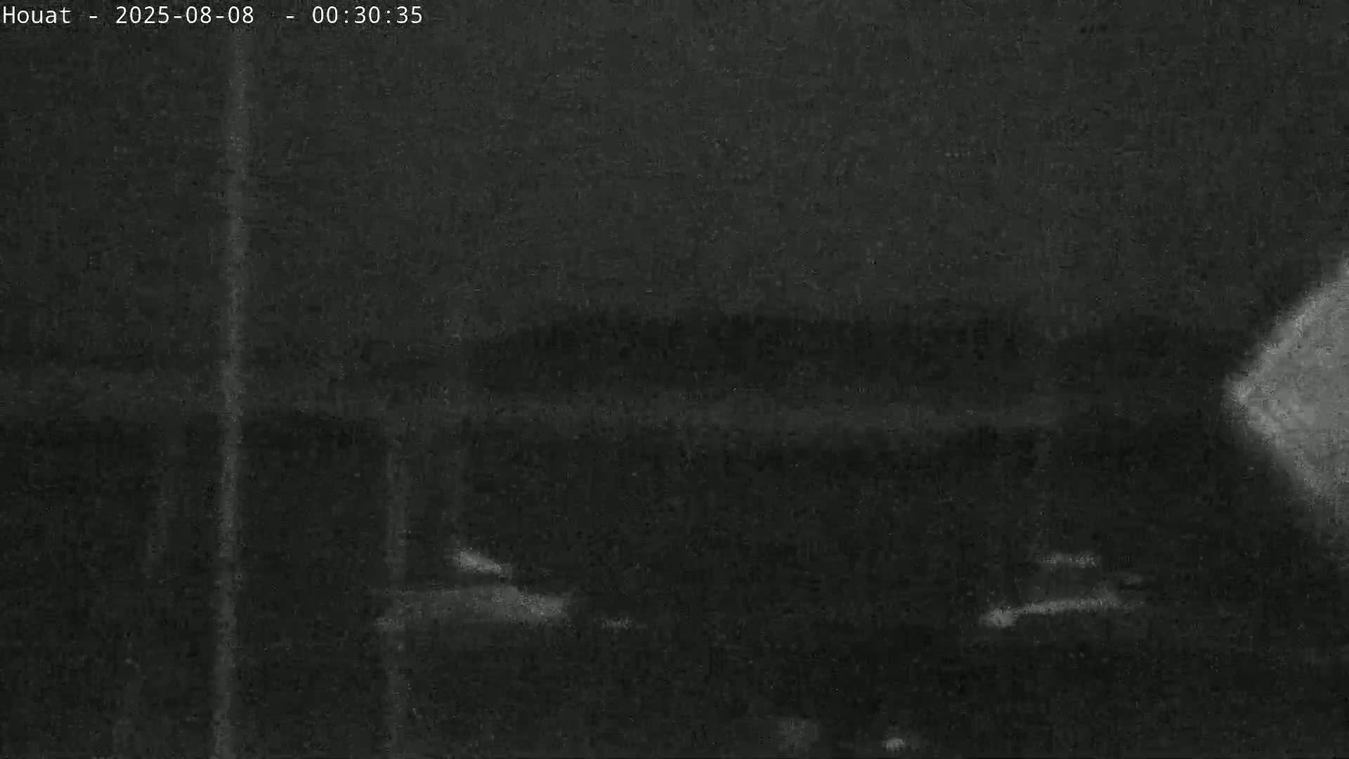 A nighttime, low-light image shows indistinct shapes suggesting vehicles or structures under a dark, possibly cloudy sky.
