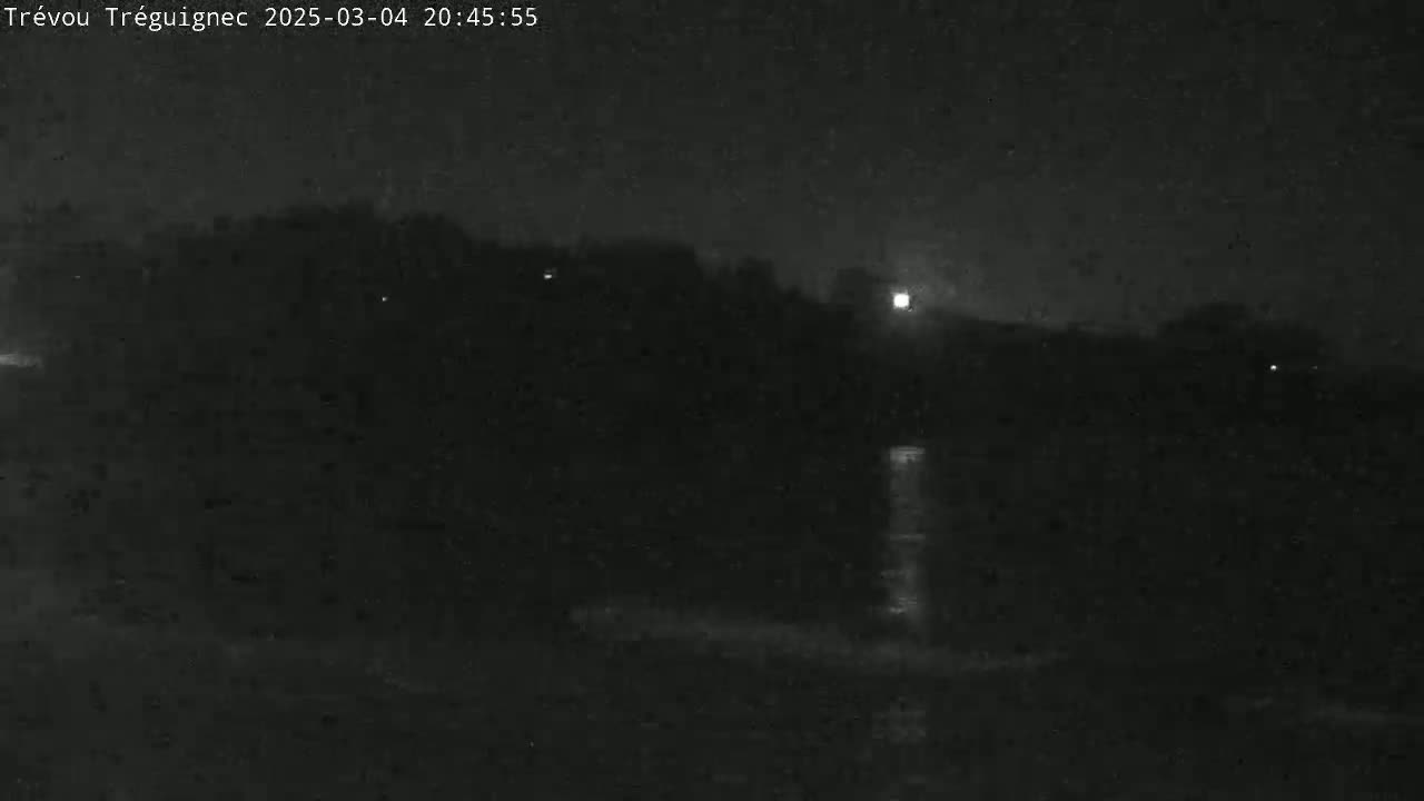 A dark, nighttime scene shows a body of water reflecting light, with a dark landmass in the background under a clear, dark sky.