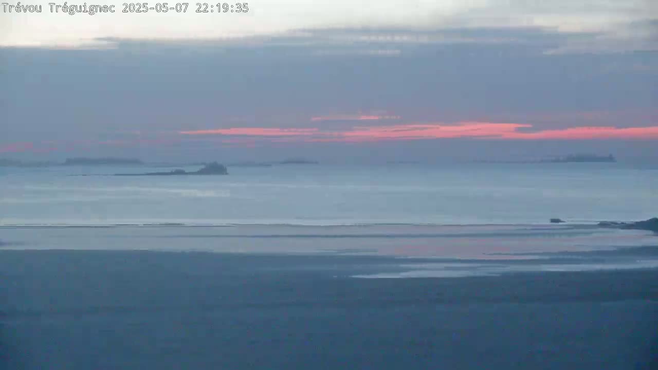 A calm body of water, with distant islands, is seen under a pale pink and gray sunset sky.