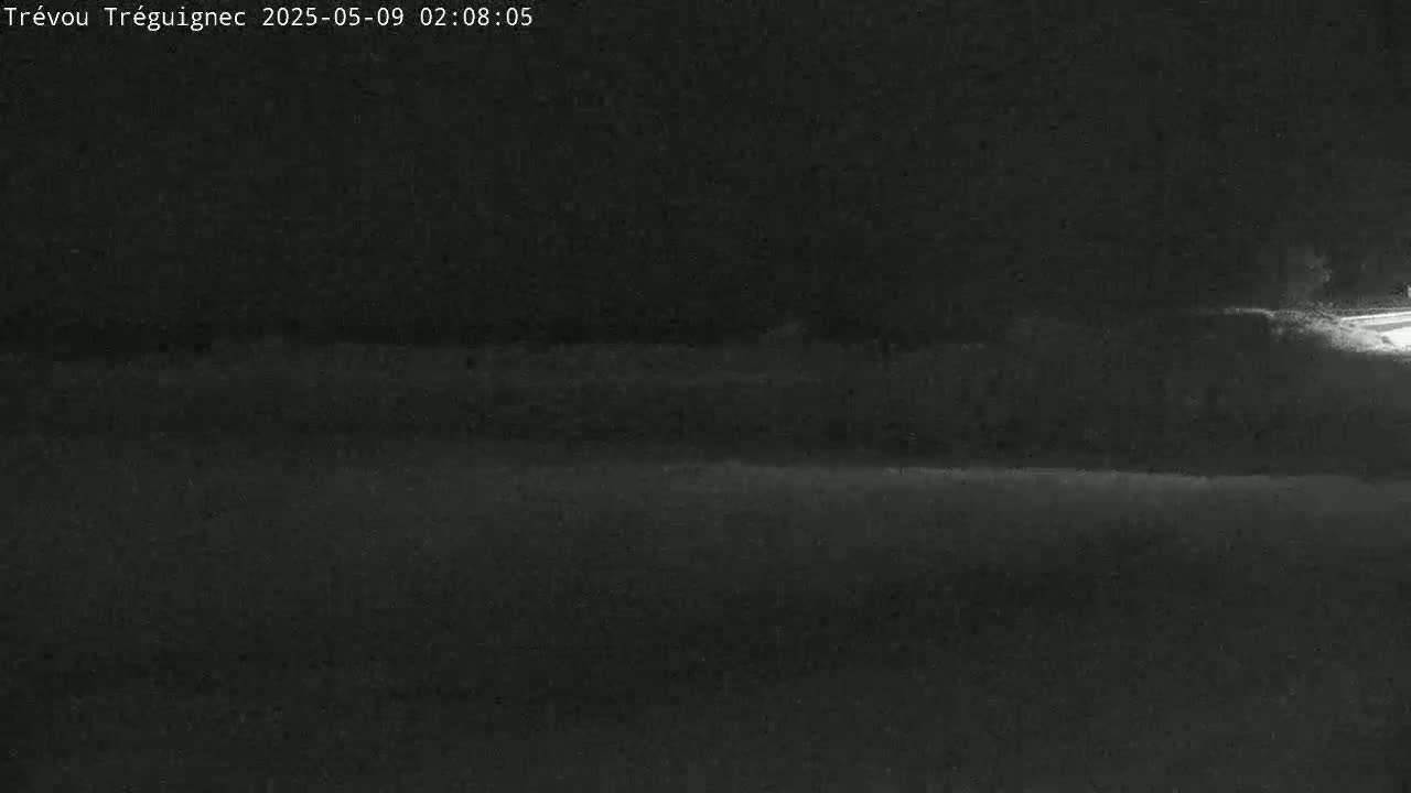 A dark, nighttime outdoor scene shows a mostly flat expanse of land with some indistinct vegetation in the distance.