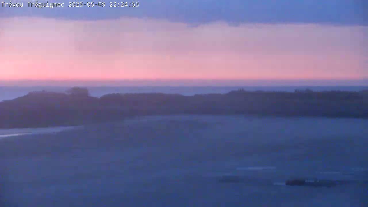 A hazy, pink and purple sunset over a calm body of water and a low-lying landmass.