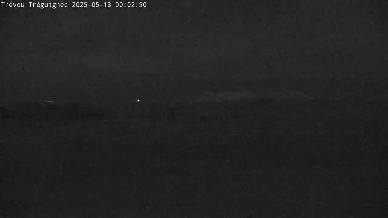 A dark, nighttime scene shows a flat, dark landscape with a few distant, faint lights.