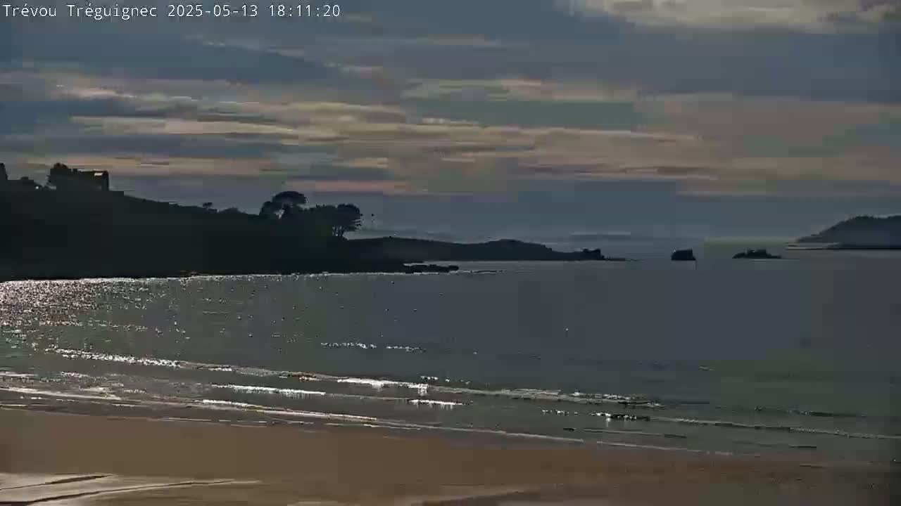 A sandy beach and calm ocean are visible under a partly cloudy sky.