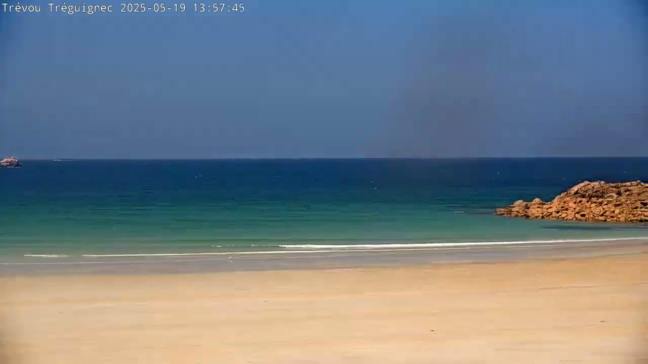 A sandy beach meets a calm, teal ocean under a clear blue sky.