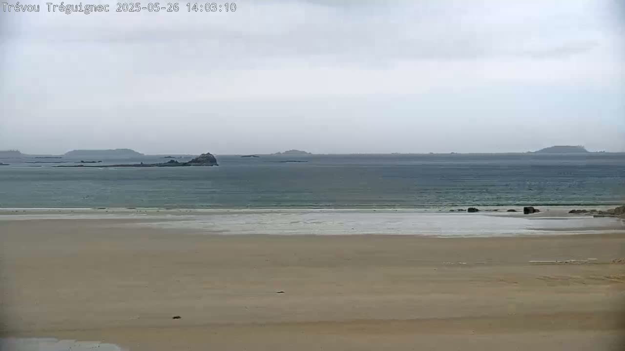 A sandy beach stretches out to a calm, gray sea with several small islands visible on the horizon under an overcast sky.