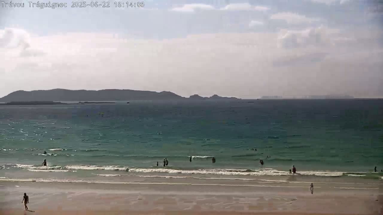 A beach with several people swimming in the ocean under a partly cloudy sky.