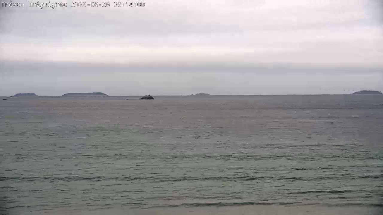 A calm, gray sea stretches to a horizon where several small, dark islands are visible under an overcast sky.