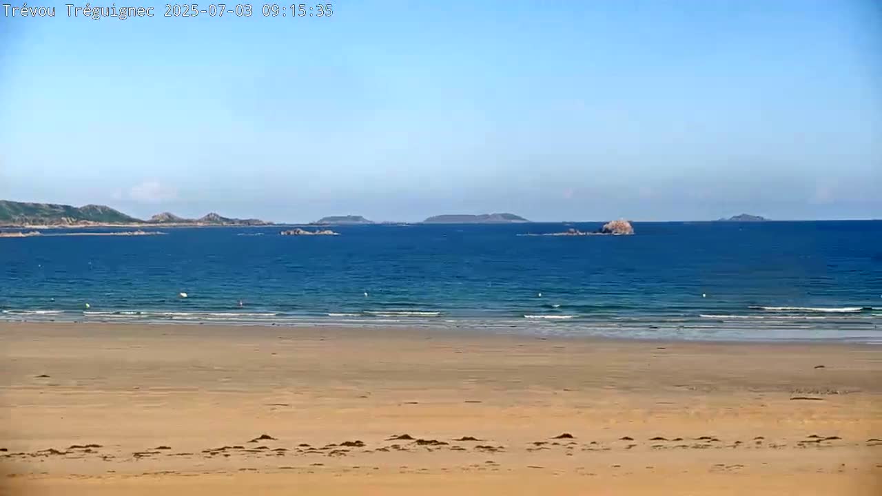 A sandy beach stretches to a calm blue ocean where small islands are visible under a clear sky.