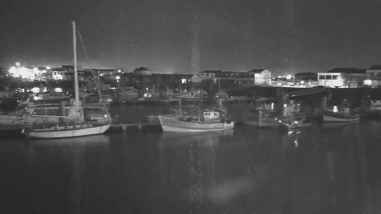 Several boats are moored in a harbor at night under a slightly snowy or dusty sky.