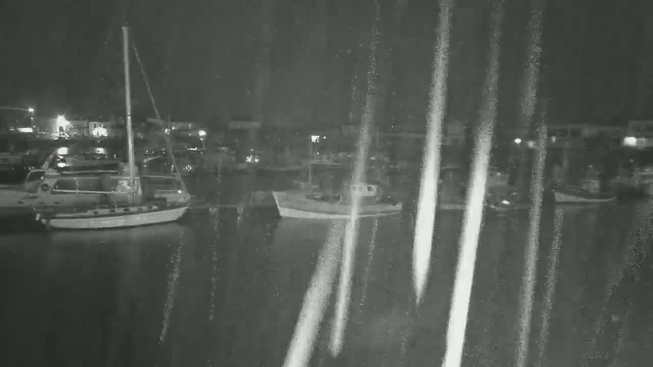 Several boats are moored in a harbor at night during a rainstorm.