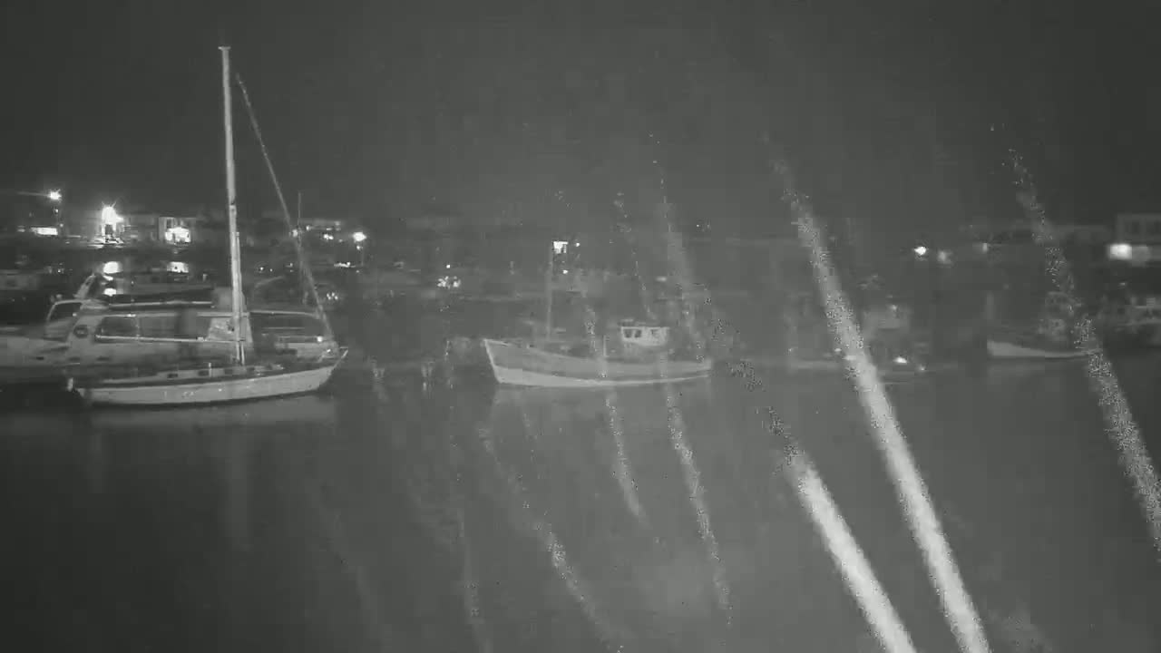 Several boats are moored in a harbor at night, under conditions of rain or light snow.
