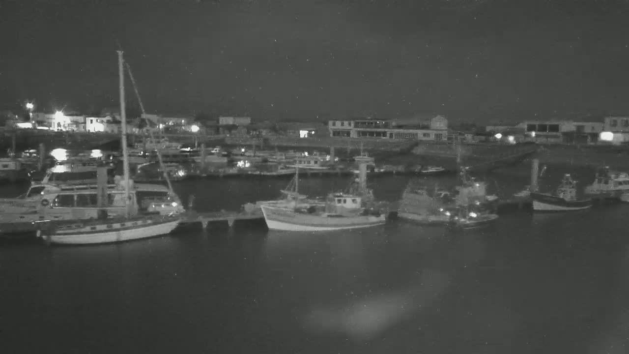 Several boats and ships are moored at a dock at night under a dark sky.