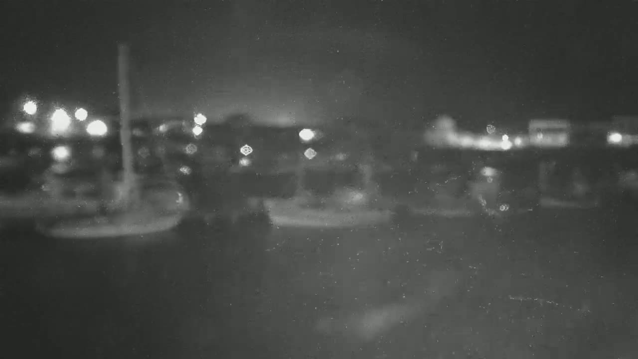 A blurry nighttime image shows out-of-focus lights and indistinct shapes, possibly vehicles or buildings, under a dark, possibly slightly snowy or dusty sky.