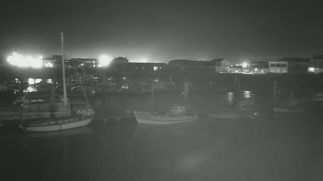 Several small boats are docked at a harbor at night under a dark sky.