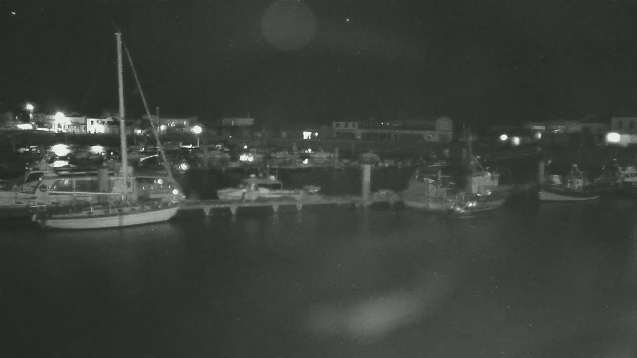 A nighttime view of a harbor with several boats moored at docks under a dark sky.