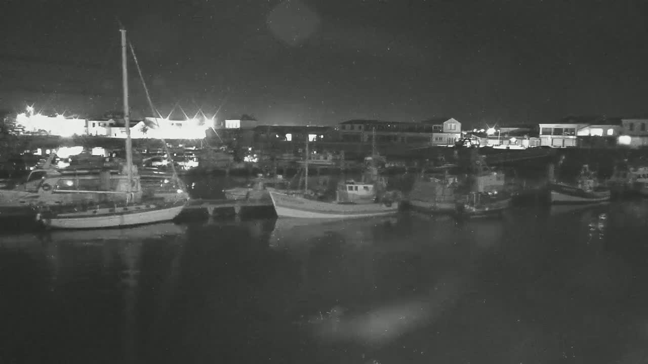 Several boats are moored at a harbor at night, under a dark sky.
