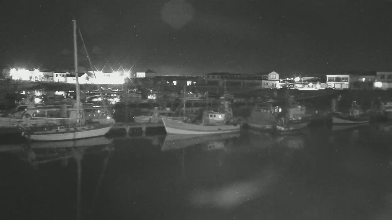 Several boats are moored in a harbor at night, their reflections visible in the calm water.