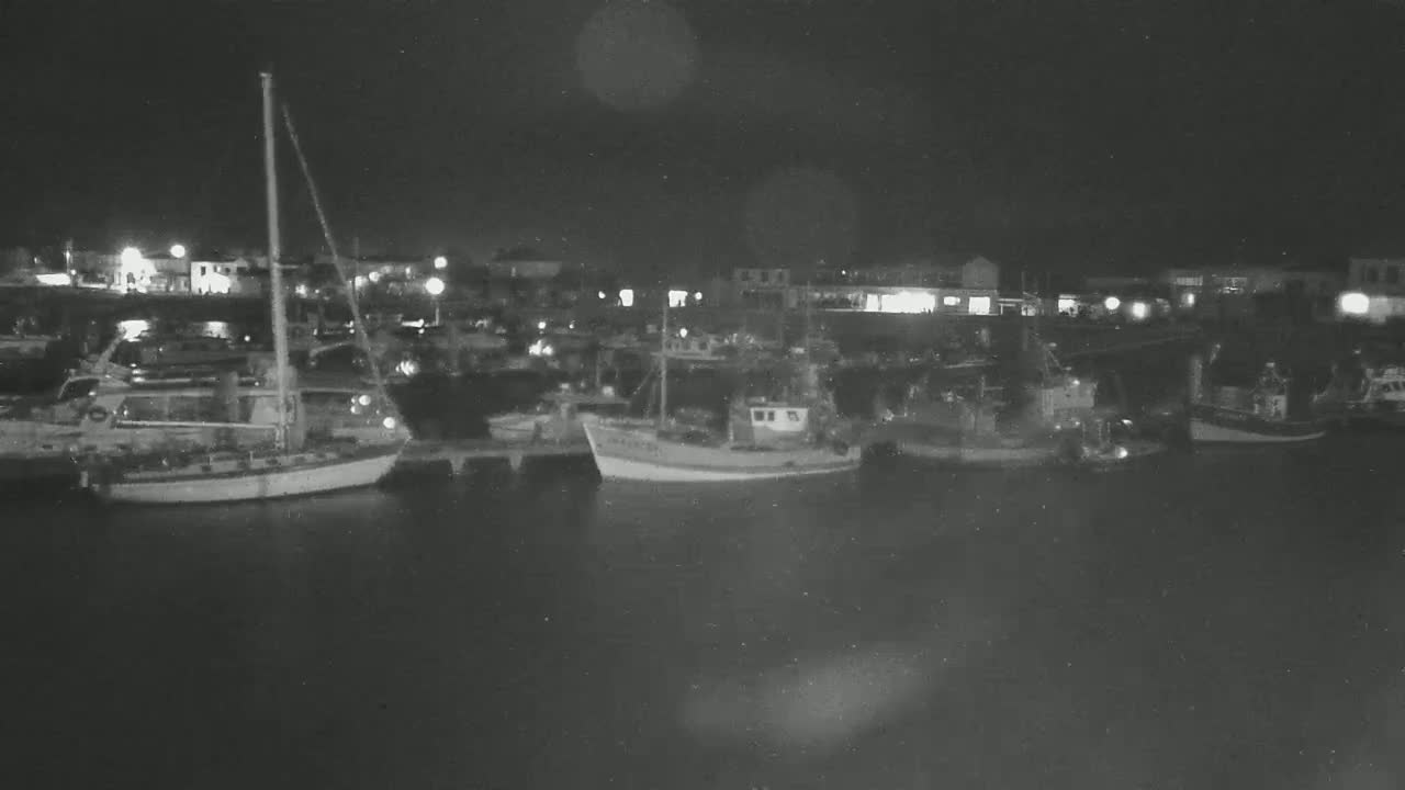 Several boats are moored at a harbor at night under a dark sky.