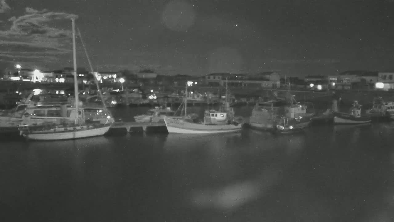 Several boats are moored in a harbor at night under a partly cloudy sky.