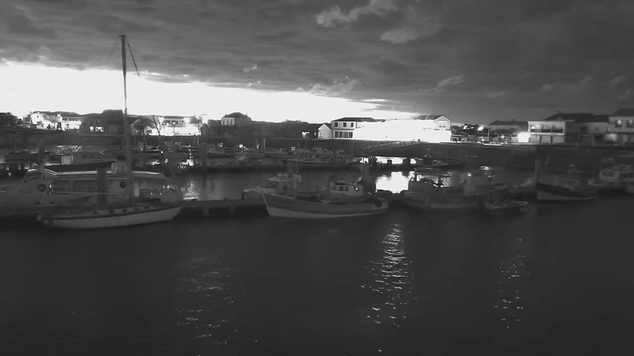 Several boats are moored in a harbor at twilight under a dark, cloudy sky.