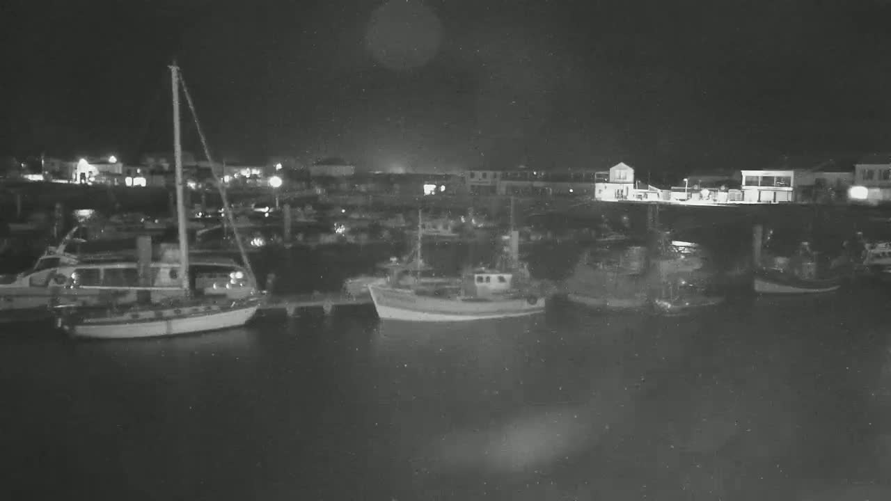 Several boats are moored at a harbor at night.