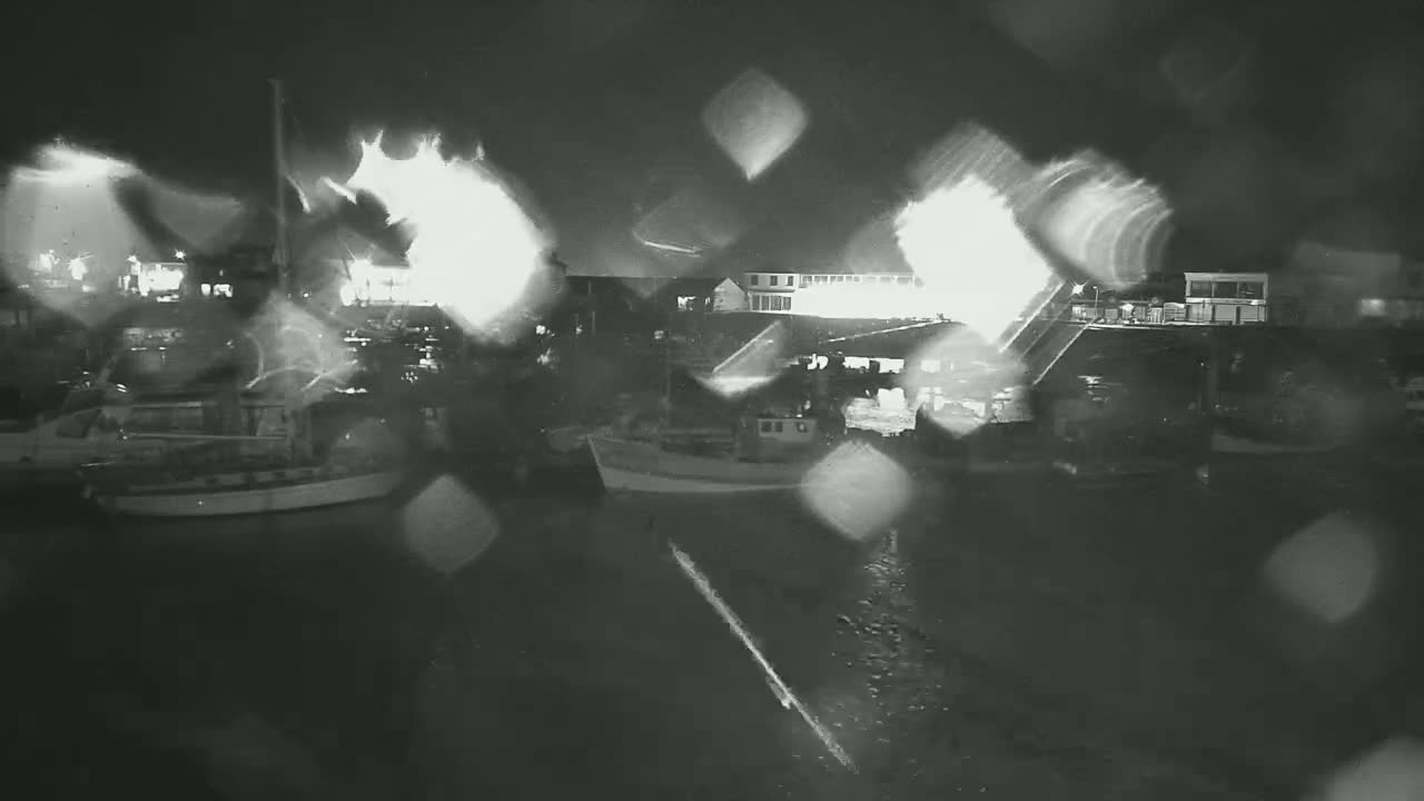 Several boats are moored at a harbor at night in the rain.