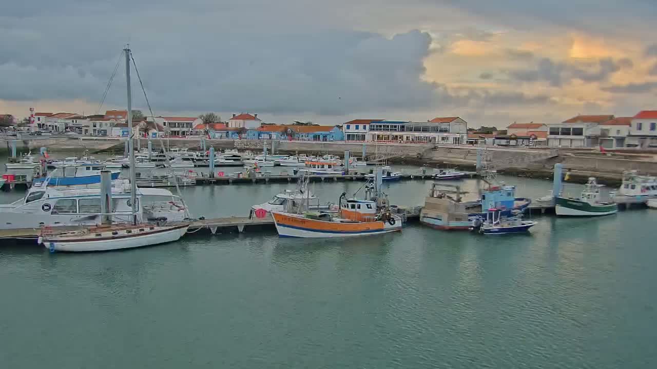 Numerous boats are docked in a harbor under a partly cloudy sky.