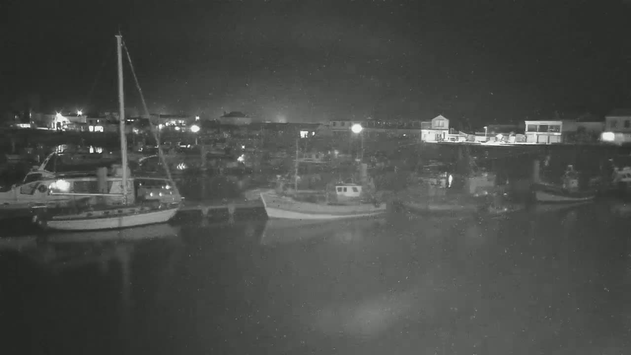 A nighttime view of a harbor filled with boats and buildings under a dark, possibly slightly snowy or dusty sky.