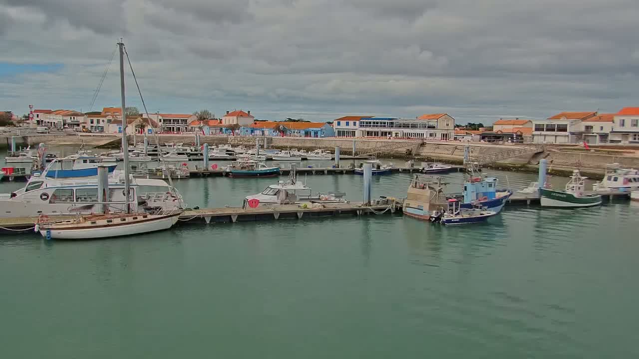 Numerous boats are docked in a harbor next to a waterfront town under a cloudy sky.