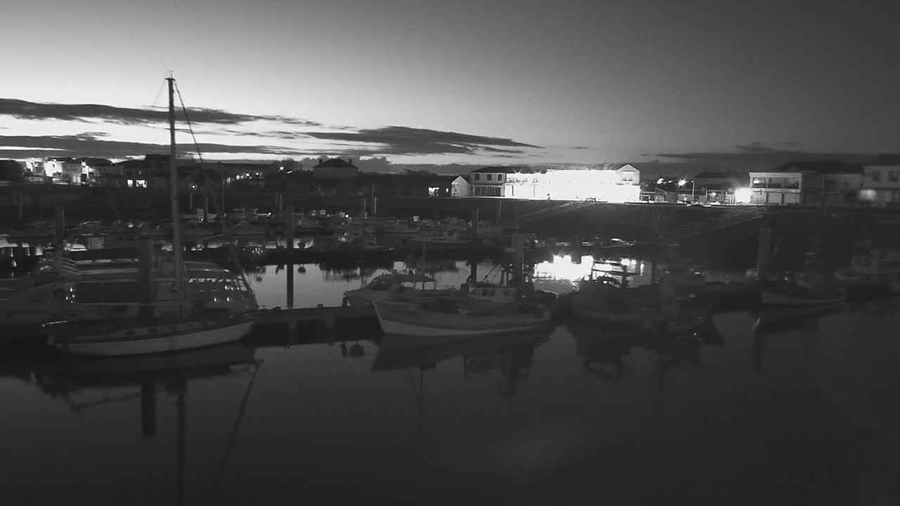 A calm harbor at twilight, filled with numerous boats moored alongside a waterfront with buildings.