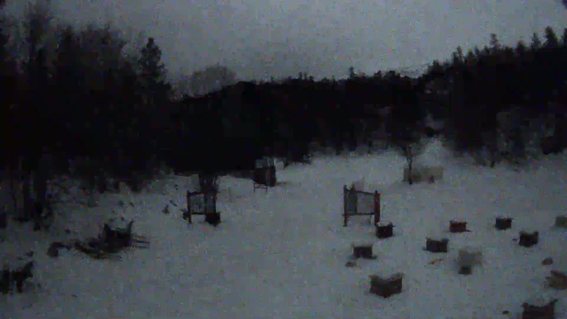 A snow-covered archery range is visible, nestled amongst dark, snow-dusted trees under a gray, overcast sky.