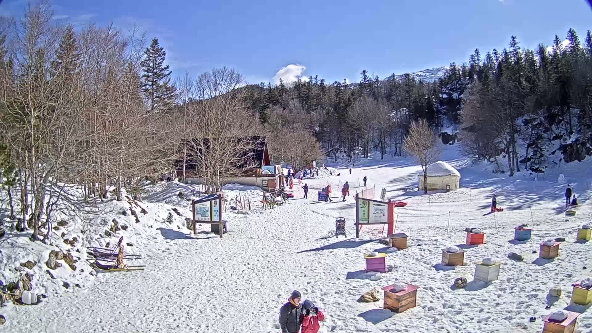 A snow-covered ski area with a small building, several people, and numerous colorful wooden boxes sits beneath a clear blue sky.